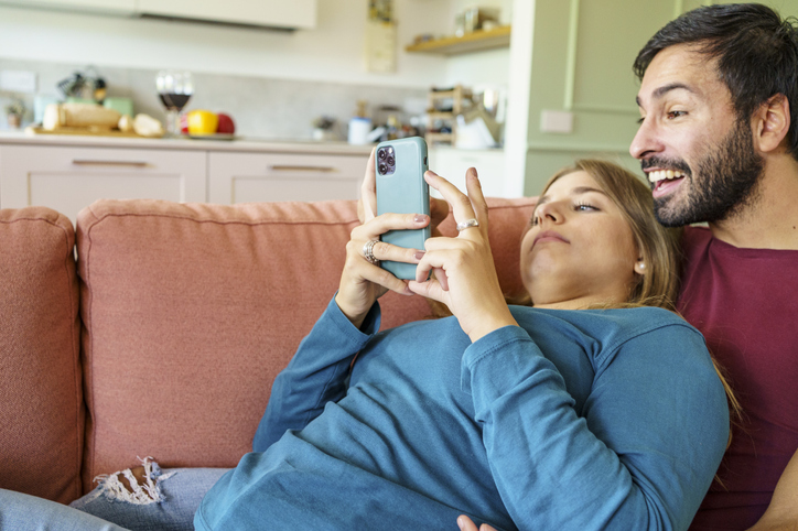 Young couple relaxing on sofa browsing social media on smartphone