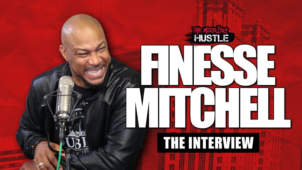 A bald man with an intense expression speaking into a microphone, with the text "The Morning Hustle" and "Finesse Mitchell: The Interview" visible.