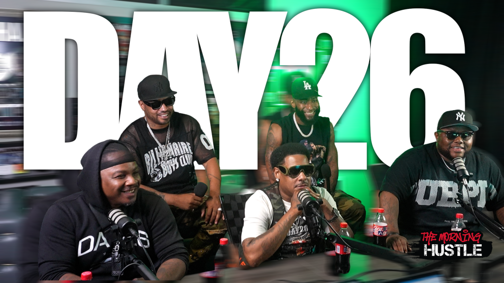 Four men wearing black clothing and hats, one holding a microphone, in front of a large "DAY26" logo on a green background.