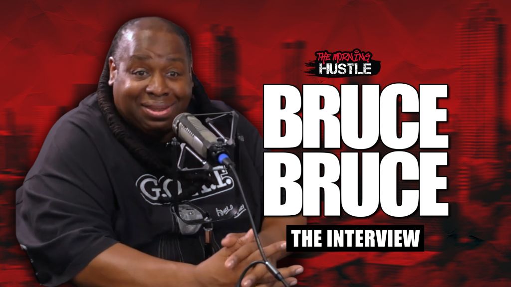 A smiling man wearing a black t-shirt with the text "Go" and holding a microphone, in front of a red background with the text "The Morning Hustle" and "Bruce Bruce The Interview".